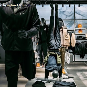 Mannequins display athletic apparel in a retail setting, with one mannequin doing a headstand. The background features shelves and clothing, while the foreground includes folded garments. Bright lighting highlights the store setup.